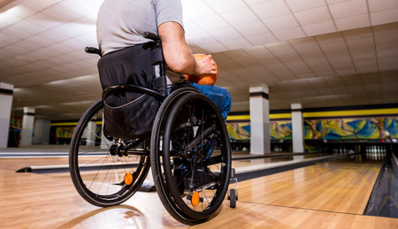 Young disabled man in wheelchair playing bowling in the club