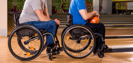 Two young disabled men in wheelchairs playing bowling in the club