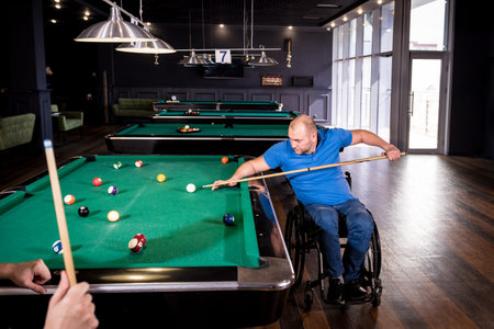 Adult men with disabilities in a wheelchair play billiards in the club