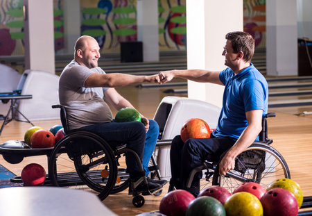 Two young disabled men in wheelchairs playing bowling in the club
