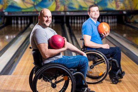 Two young disabled men in wheelchairs playing bowling in the club