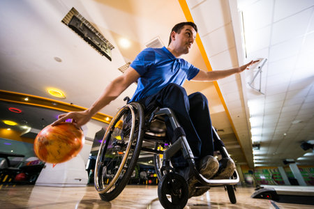 Young disabled man in wheelchair playing bowling in the clubの写真素材
