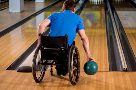 Young disabled man in wheelchair playing bowling in the clubの写真素材