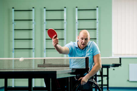 Adult disabled man in a wheelchair play at table tennis with his coachの写真素材