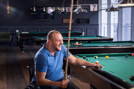 Adult man with disability in a wheelchair play billiards in the clubの写真素材