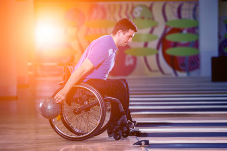 Young disabled man in wheelchair playing bowling in the clubの写真素材