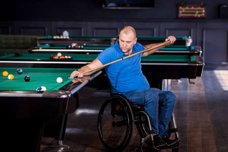 Adult man with disability in a wheelchair play billiards in the clubの写真素材
