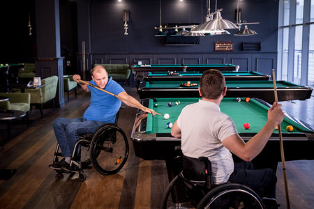 Adult men with disabilities in a wheelchair play billiards in the club