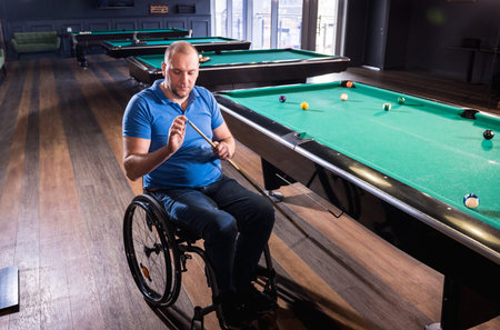 Adult man with disability in a wheelchair play billiards in the club