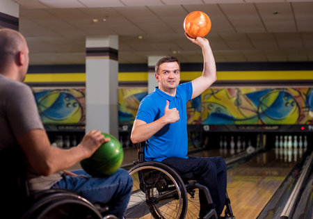 Two young disabled men in wheelchairs playing bowling in the club