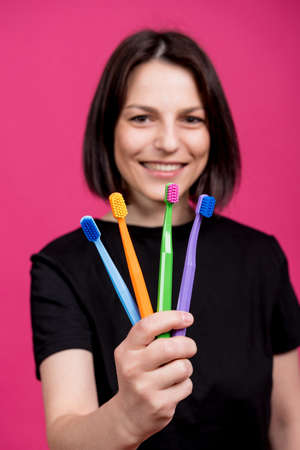 Beautiful happy young woman with different colored toothbrushes on blank pink backgroundの写真素材