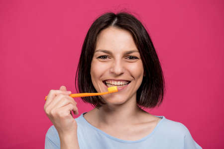 Beautiful happy young woman with toothbrush on blank pink backgroundの写真素材