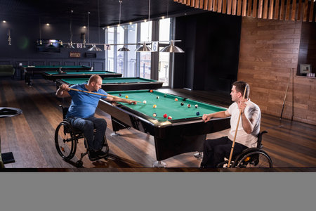 Adult men with disabilities in a wheelchair play billiards in the club