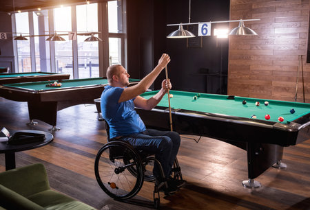 Adult man with disability in a wheelchair play billiards in the club