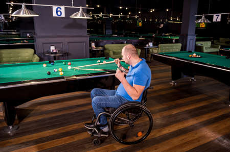 Adult man with disability in a wheelchair play billiards in the clubの写真素材
