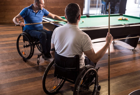 Adult men with disabilities in a wheelchair play billiards in the club