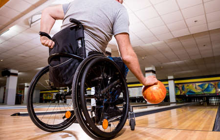 Young disabled man in wheelchair playing bowling in the clubの写真素材