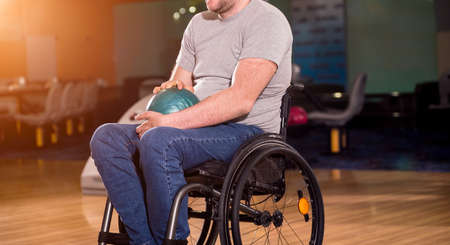 Young disabled man in wheelchair playing bowling in the clubの写真素材