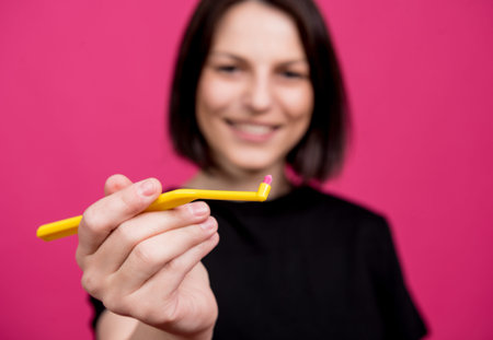 Beautiful happy young woman with single tufted toothbrush on blank pink background