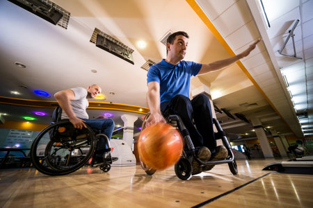 Two young disabled men in wheelchairs playing bowling in the clubの写真素材