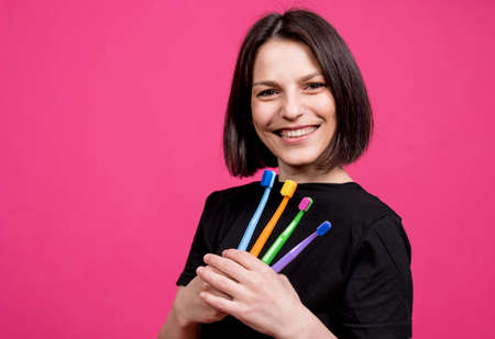 Beautiful happy young woman with different colored toothbrushes on blank pink backgroundの写真素材