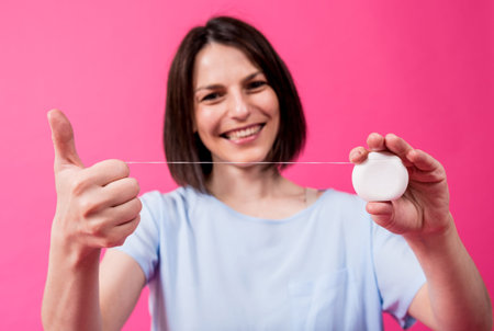 Beautiful young woman use dental floss on pink background