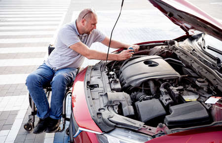 Disabled man in wheelchair check engine his car at parkingの写真素材