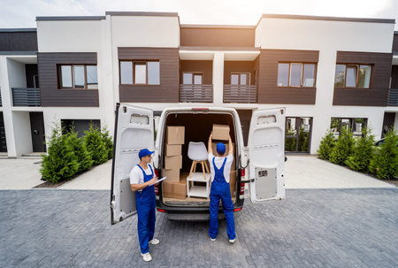Two removal company workers are loading boxes and furniture into a minibus.の写真素材
