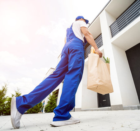 Young courier wearing a protective mask and gloves delivers goods during quarantineの写真素材