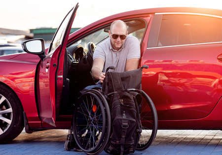 Young handicapped driver getting in red car fom wheelchairの写真素材