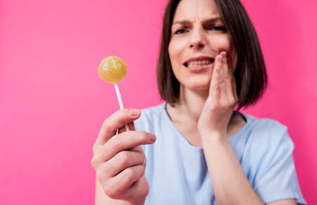 Young woman with sensitive teeth eating sweet lollipop on color backgroundの写真素材
