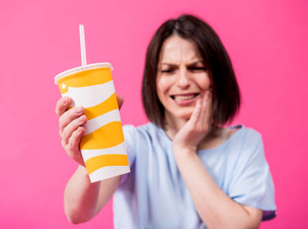 Young woman with sensitive teeth drinking cold water on color backgroundの写真素材