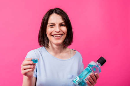Beautiful girl uses mouthwash on the pink backgroundの写真素材