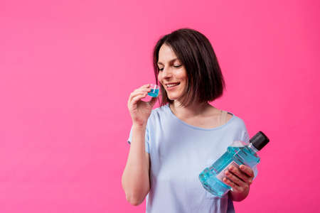 Beautiful girl uses mouthwash on the pink backgroundの写真素材