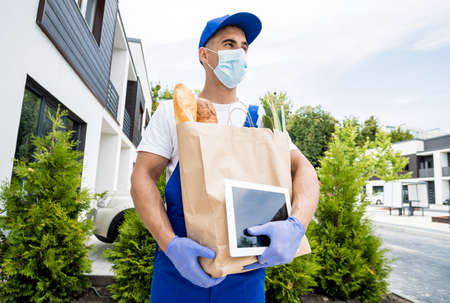 Young courier wearing a protective mask and gloves delivers goods during quarantineの写真素材