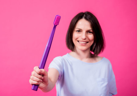 Beautiful happy young woman with big toothbrush on blank pink background