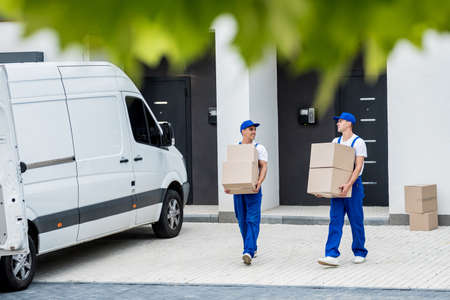 Two removal company workers are loading boxes and furniture into a minibus.の写真素材