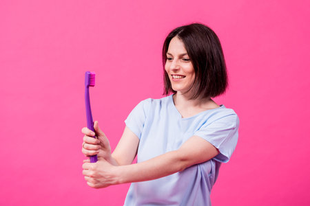 Beautiful happy young woman with big toothbrush on blank pink backgroundの写真素材