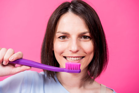 Beautiful happy young woman with big toothbrush on blank pink background