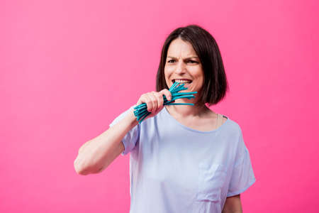 Young woman with sensitive teeth eating sweet candies on color backgroundの写真素材