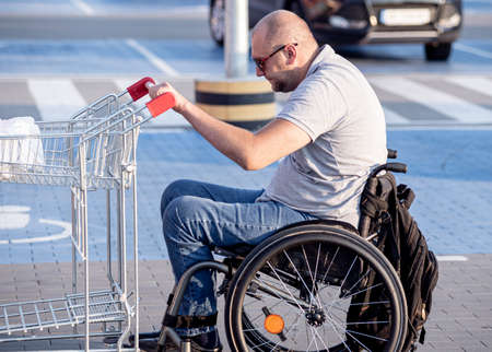 Person with a physical disability pushing cart in front of himself at supermarket parkingの写真素材
