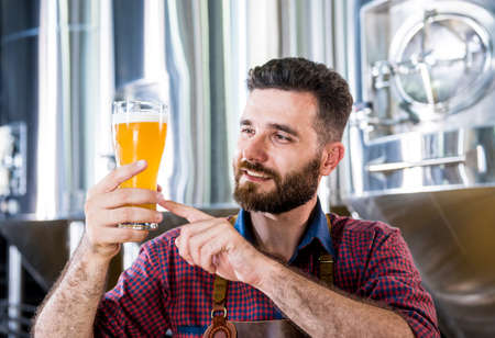 Young brewer wearing a leather apron is testing beer at a modern breweryの写真素材