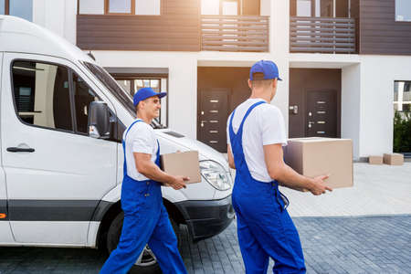 Two removal company workers unloading boxes from minibus into new homeの写真素材