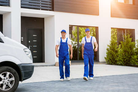 Two removal company workers unloading boxes from minibus into new homeの写真素材