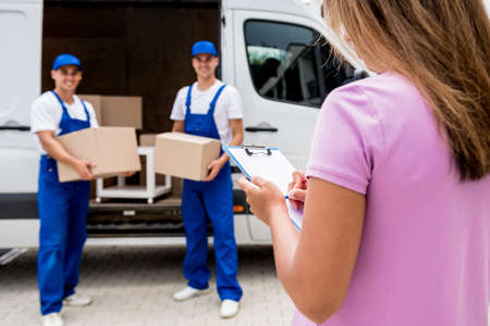 Two removal company workers unloading boxes from minibus into customers homeの写真素材