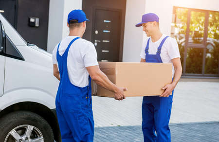 Two removal company workers unloading boxes from minibus into new homeの写真素材