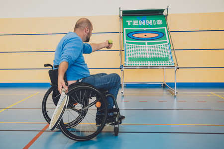Adult man with a physical disability in a wheelchair playing tennis on indoor tennis courtの写真素材