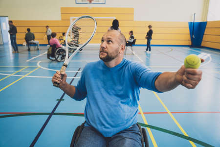 Adult man with a physical disability in a wheelchair playing tennis on indoor tennis courtの写真素材
