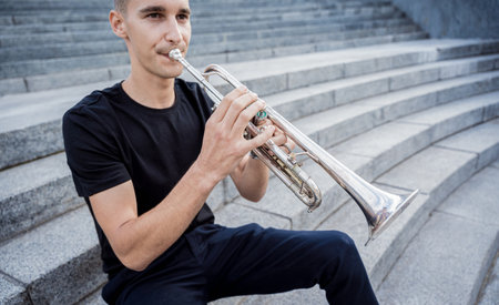 Young street musician playing guitar sitting on granite stepsの写真素材