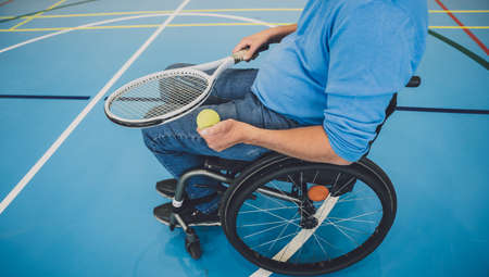 Adult man with a physical disability in a wheelchair playing tennis on indoor tennis courtの写真素材